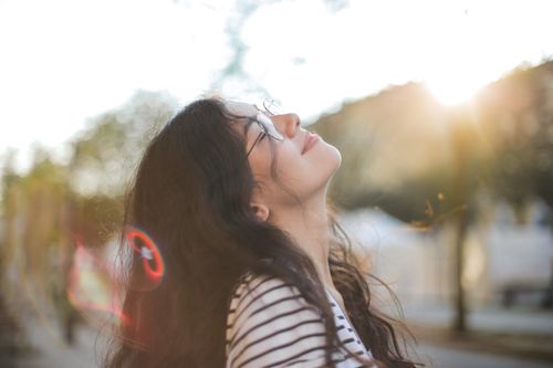 Free A woman in a striped shirt enjoys sunlight with closed eyes and a smile outdoors. Stock Photo
