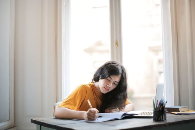 A woman writing at a desk by a window