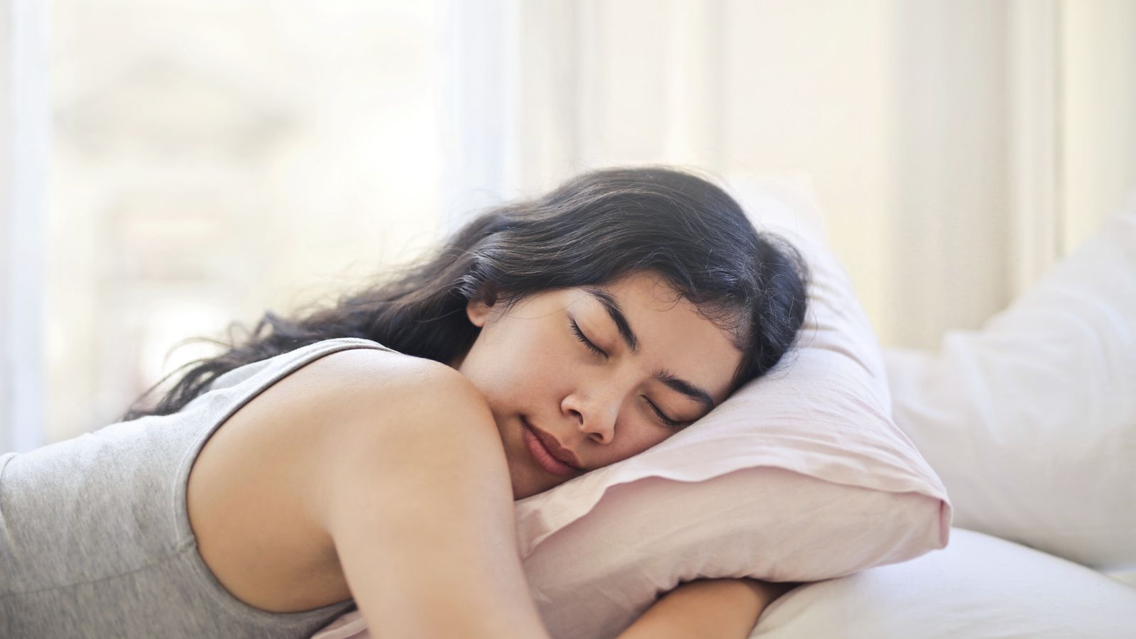 Serene woman resting on a comfortable bed with soft pillows and natural light.