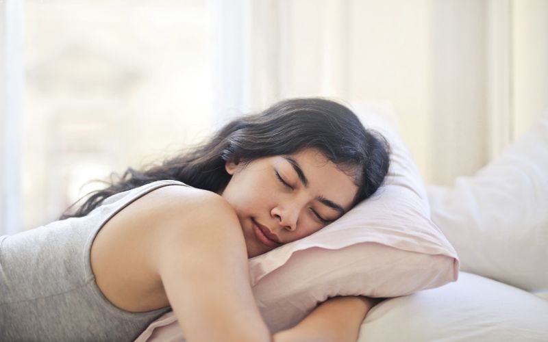 Serene woman resting on a comfortable bed with soft pillows and natural light.
