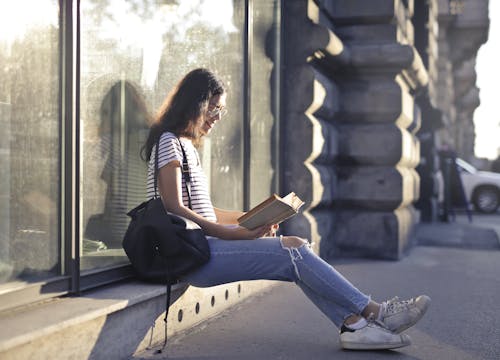 Женщина сидит у стеклянной стены во время чтения книги