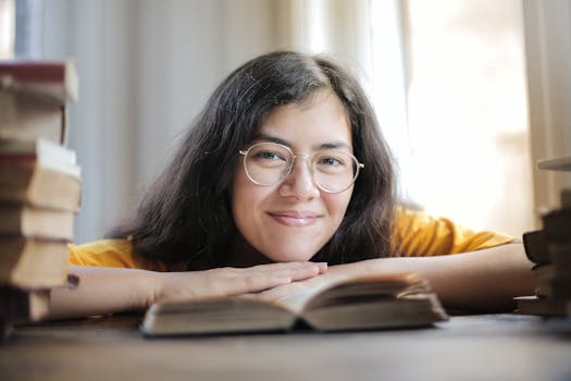 一名戴眼镜的女子微笑着，将头靠在一本书上，周围摆满了更多的书