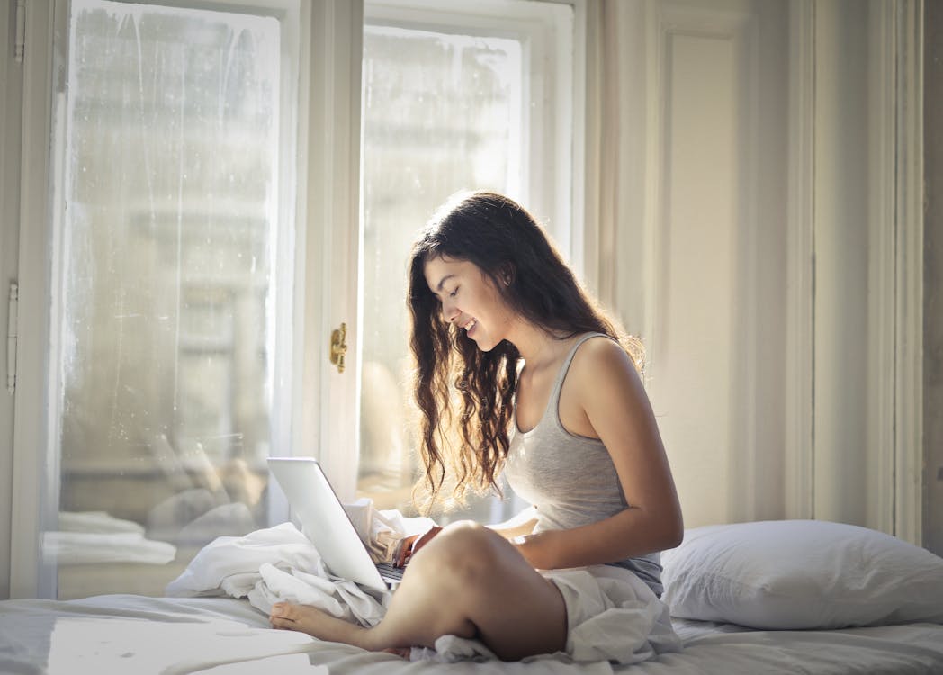 Free Woman in Gray Tank Top Sitting on Bed Stock Photo