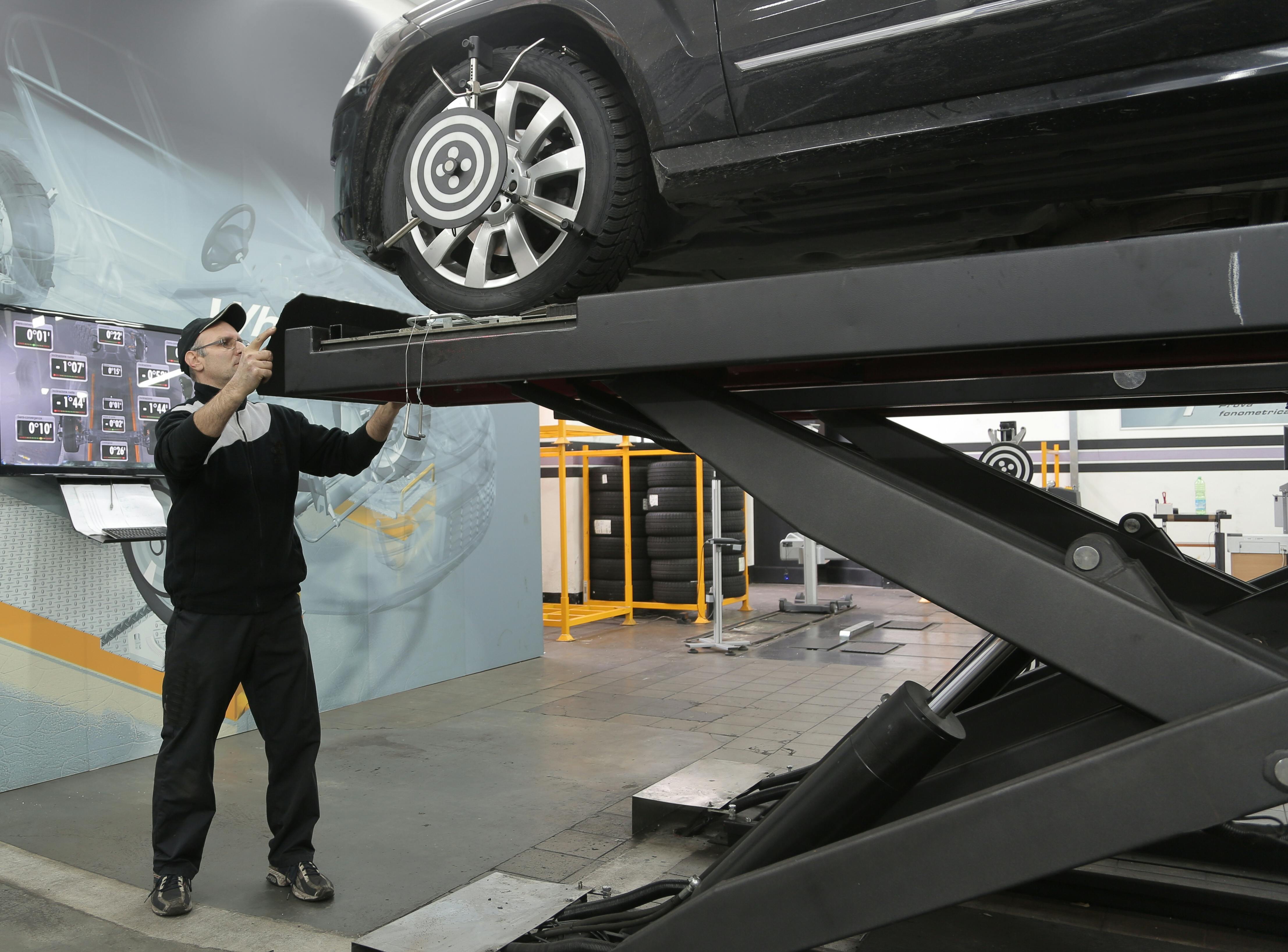 serious mechanic checking car wheels on lift in modern car service garage