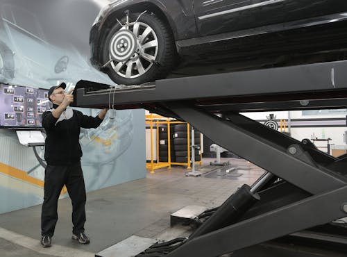 Serious mechanic checking car wheels on lift in modern car service garage