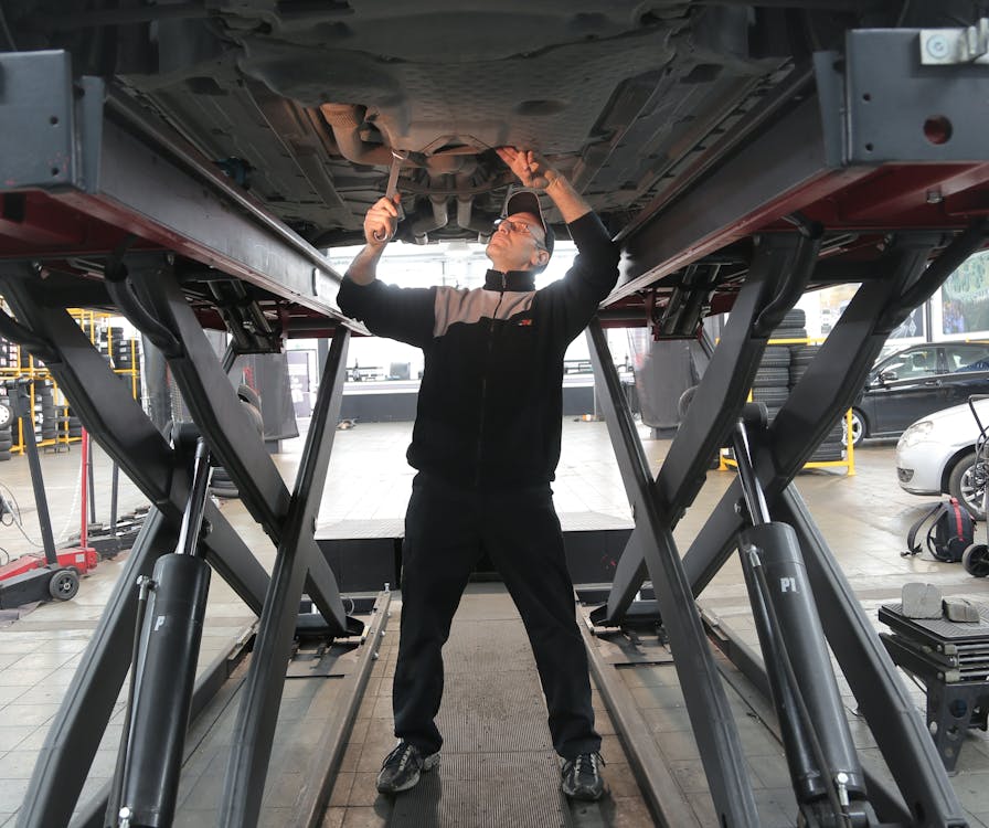 Free Man in Black Jacket and Black Pants Standing Under Vehicle Stock Photo