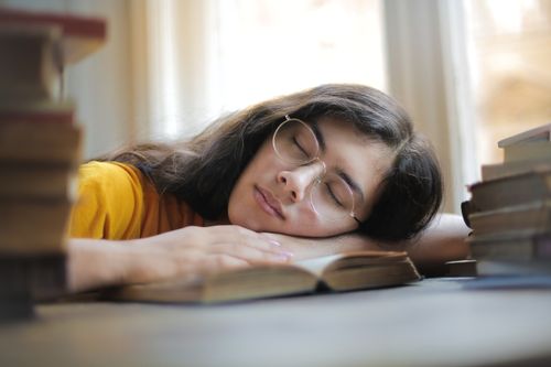 Free A young woman with glasses naps on a book indoors during the day, capturing a moment of relaxation and fatigue. Stock Photo