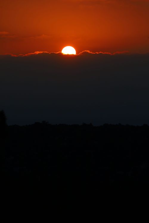 Free Vibrant sunset with half sun hidden by clouds creating dramatic colors. Stock Photo