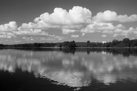 Serene black and white landscape of a reflective lake under fluffy clouds in Jönköping, Sweden.