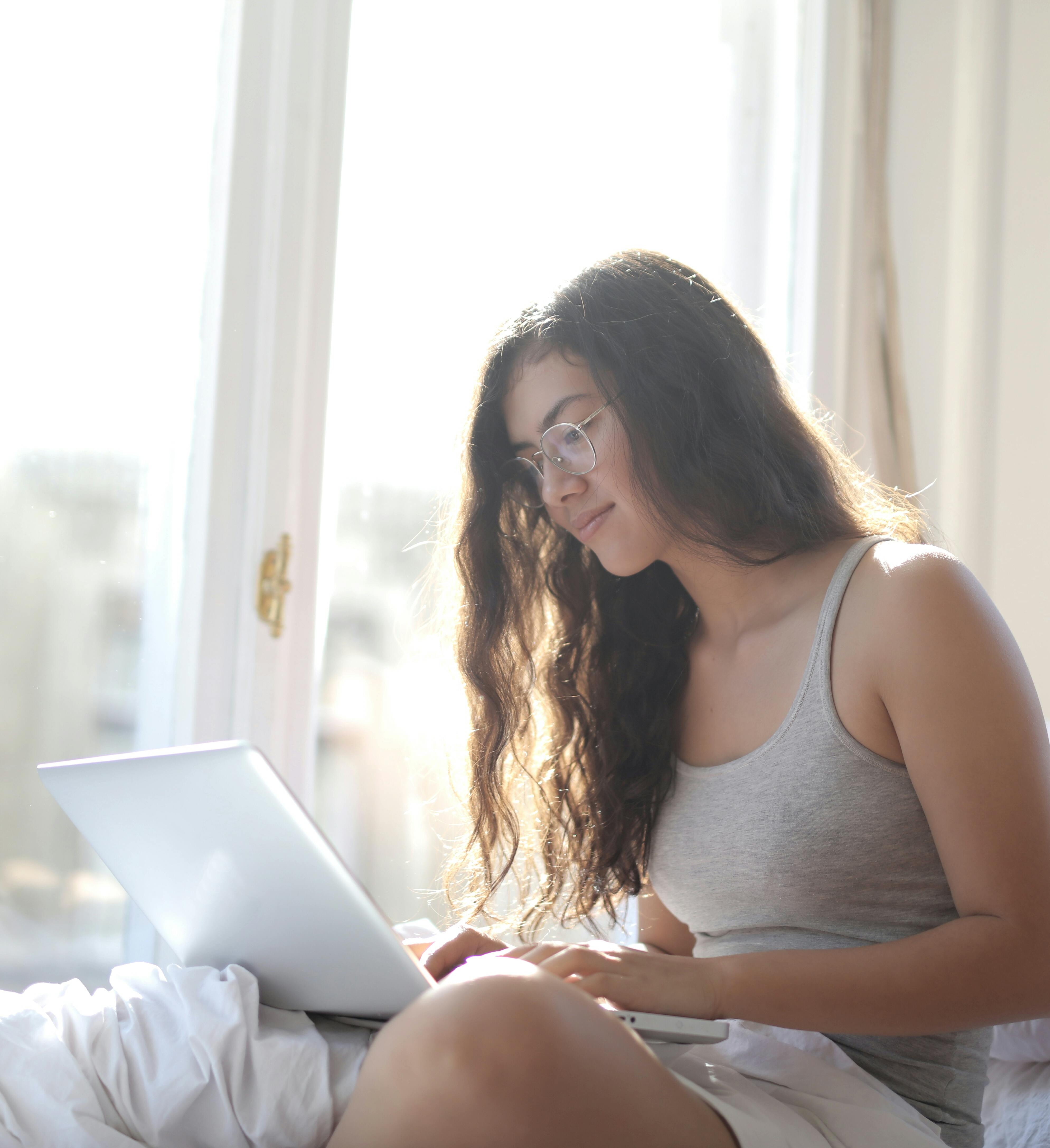 glad woman typing on laptop in bed