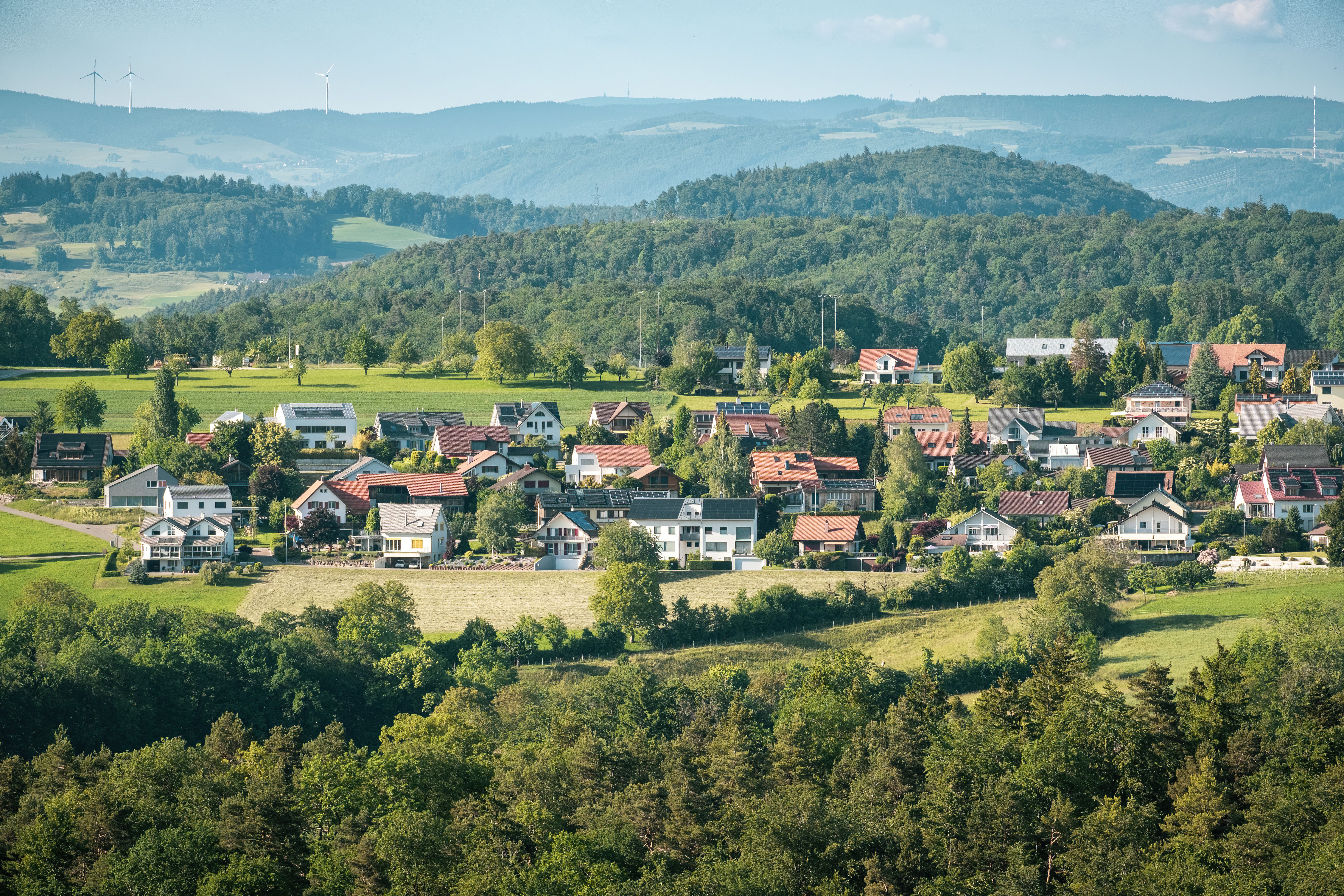Picturesque village nestled in lush green hills with scenic views and wind turbines.