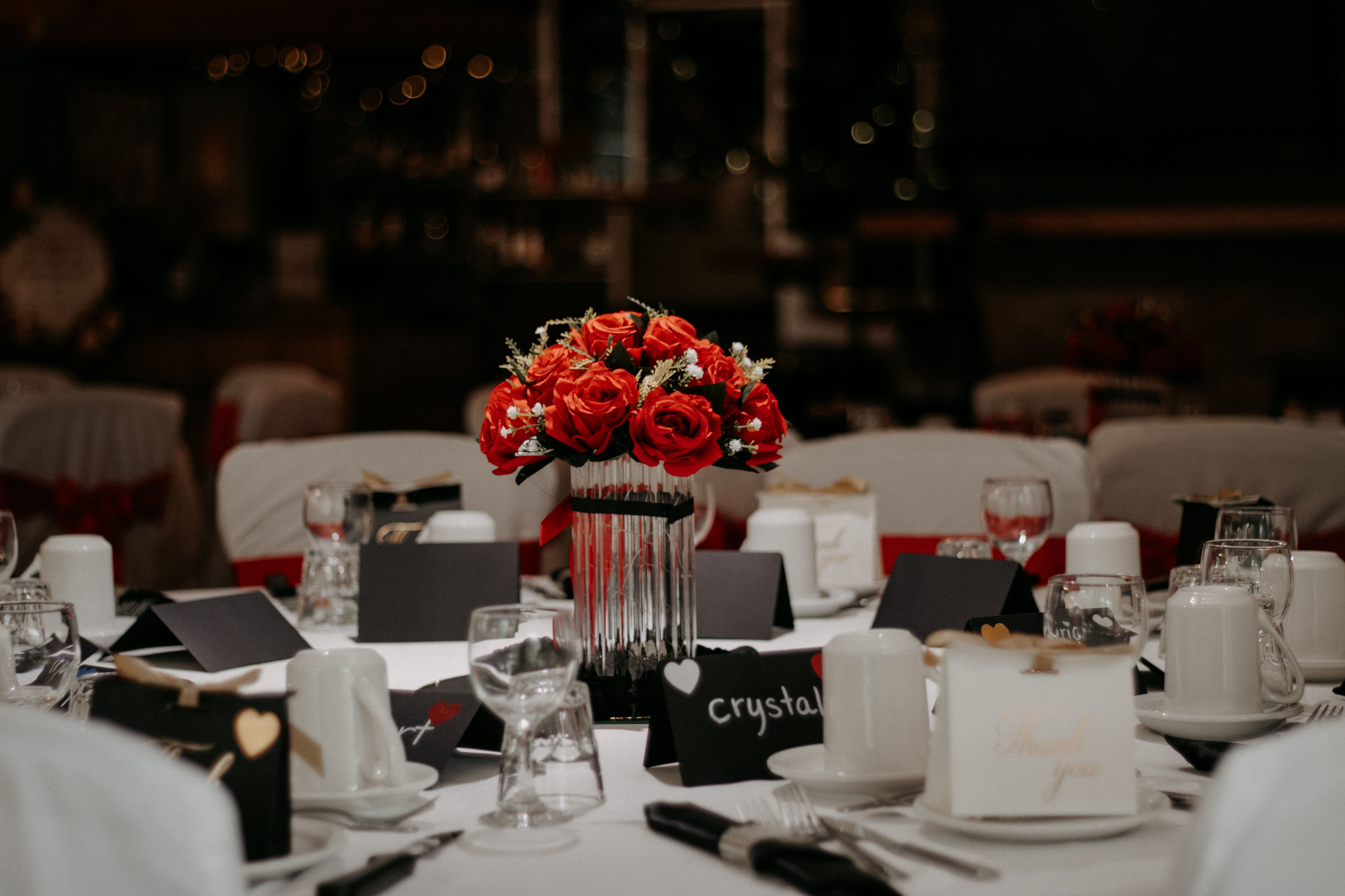Beautifully decorated wedding table with red roses and elegant dinnerware under soft lighting.