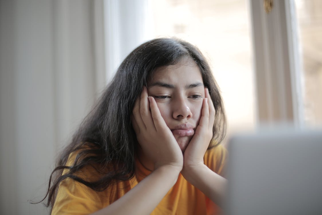 Free Bored ethnic female in casual clothes sitting at table with netbook and watching sad movie while resting at home during weekend Stock Photo
