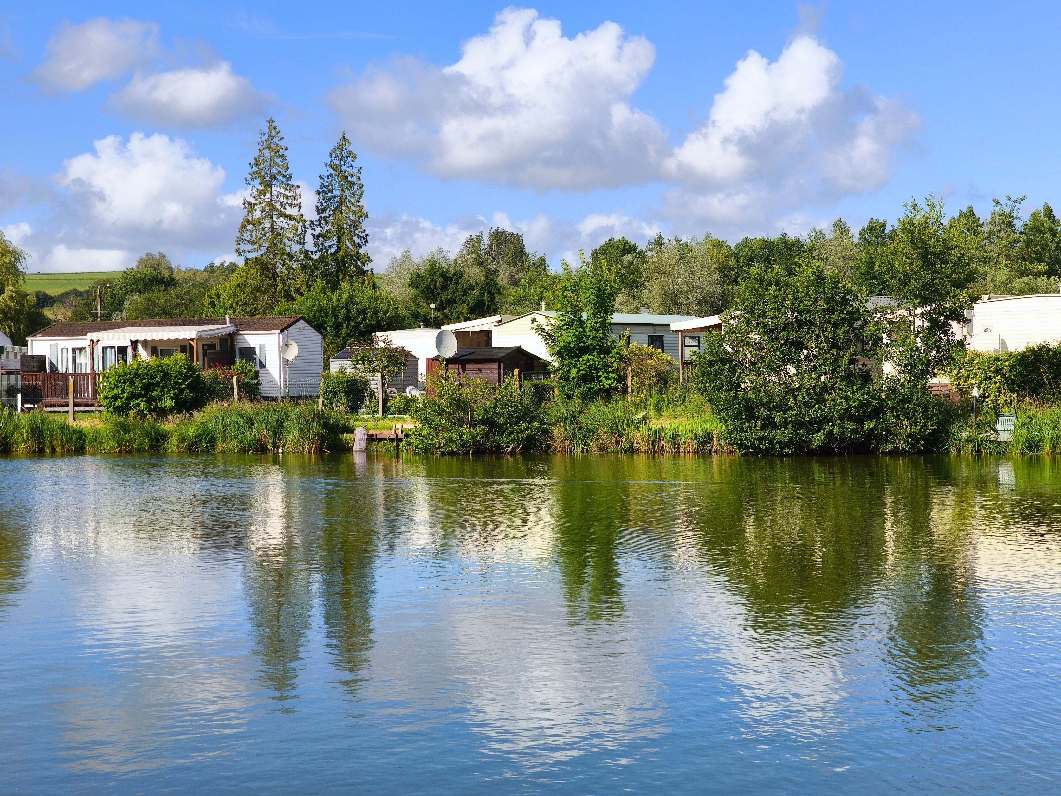 Beautiful lakeside scene with reflections of mobile homes and trees under a clear summer sky.