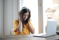 一位戴着耳机的年轻女子坐在办公桌前，对着笔记本电脑听音乐，展现了远程工作的生活方式