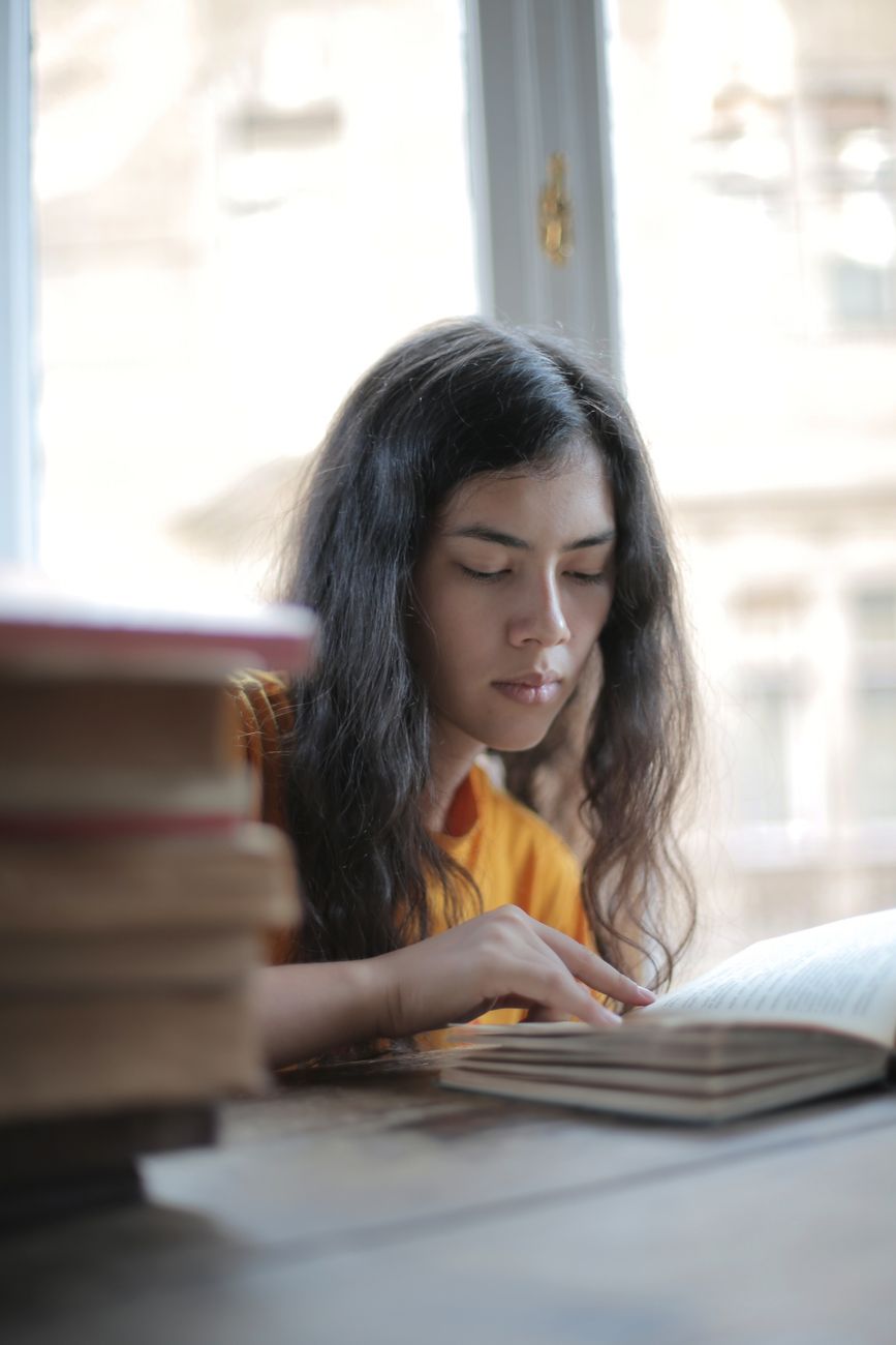 Focused young woman reading a book in a cozy indoor setting by the window.. focused, young, woman