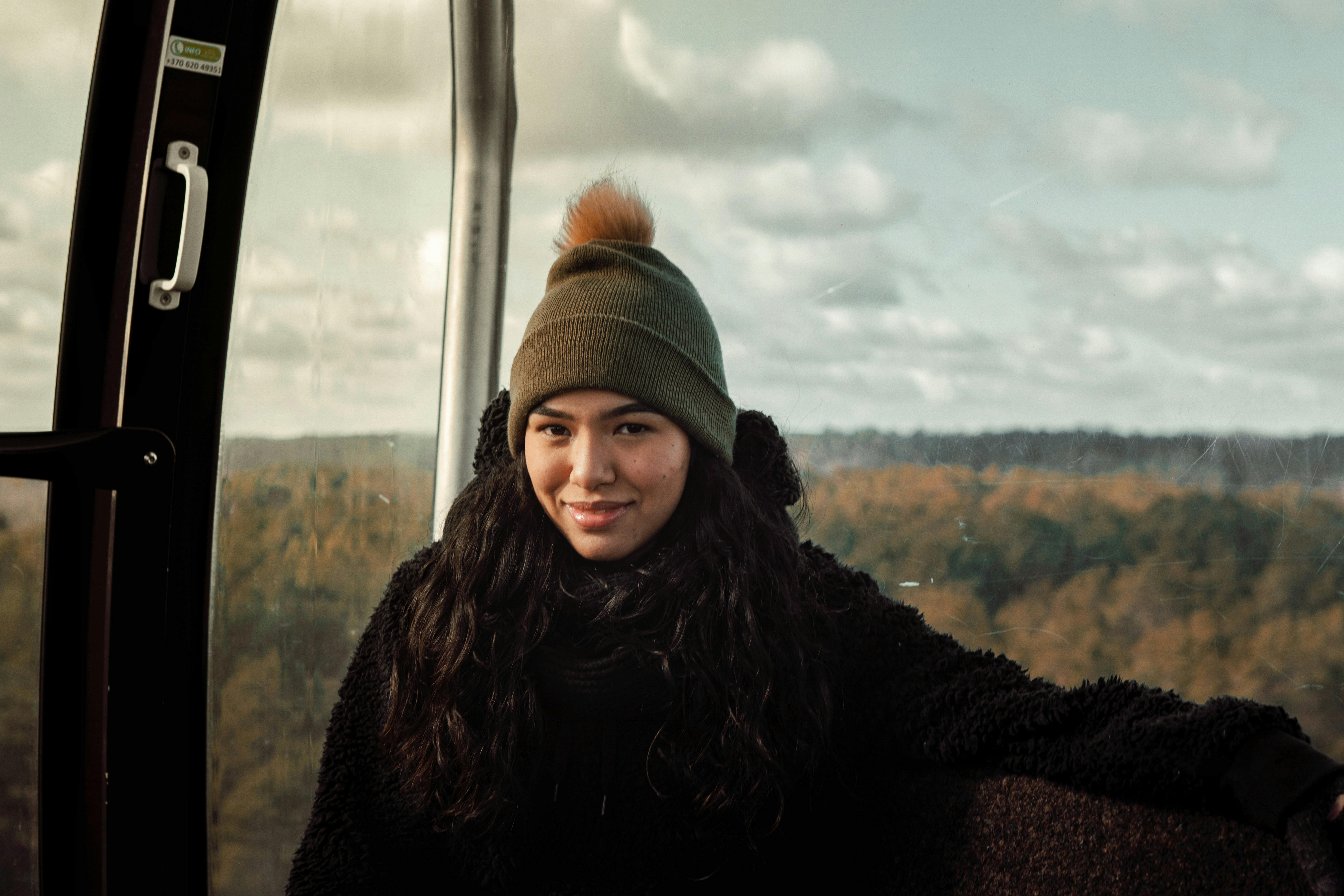 Smiling woman in a beanie enjoying a gondola ride over autumn forests in Lithuania.