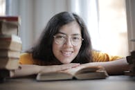 戴着眼镜的快乐女人在室内读书时微笑，周围都是书籍