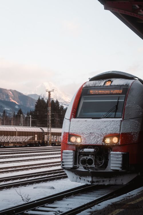 Free Red train covered with snow at Bad Aussee Station in Austria, showcasing winter landscape and mountains. Stock Photo