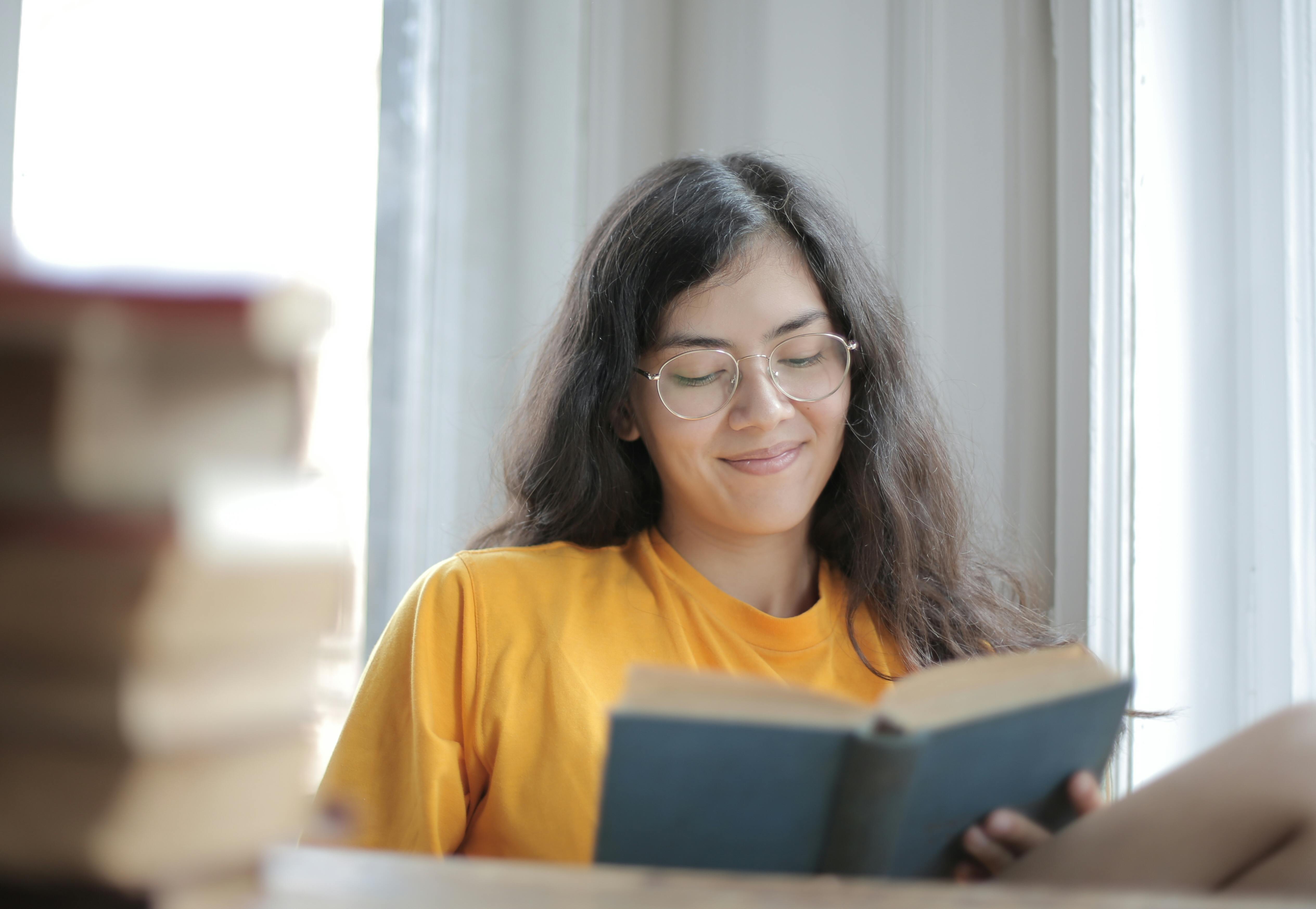 Woman in Yellow Shirt Smiling While Reading a Book · Free Stock Photo