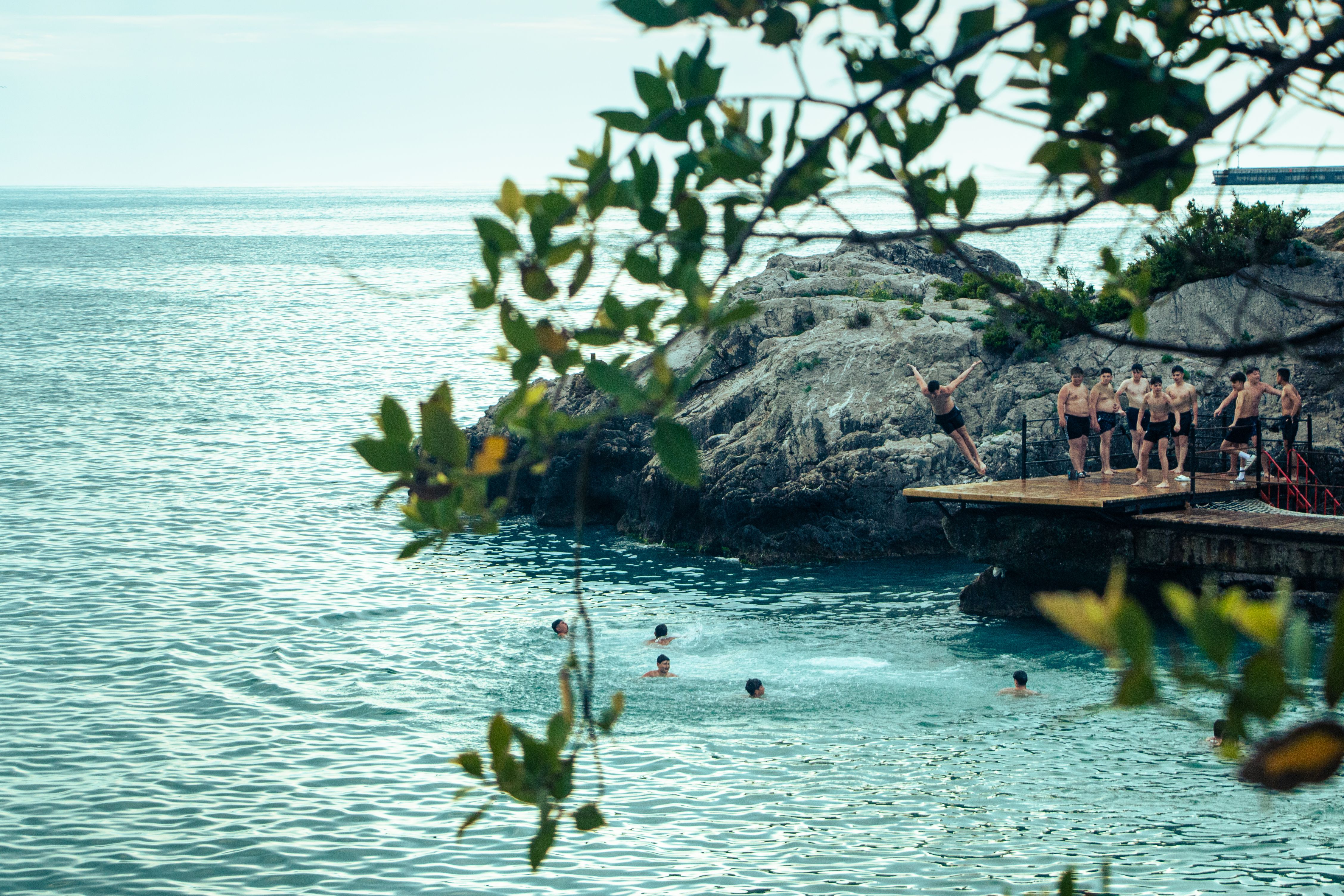 A lively scene of people cliff diving and swimming in turquoise waters on a sunny day.