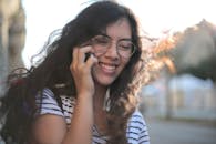 一位戴眼镜的年轻女子在阳光明媚的城市户外微笑着打电话