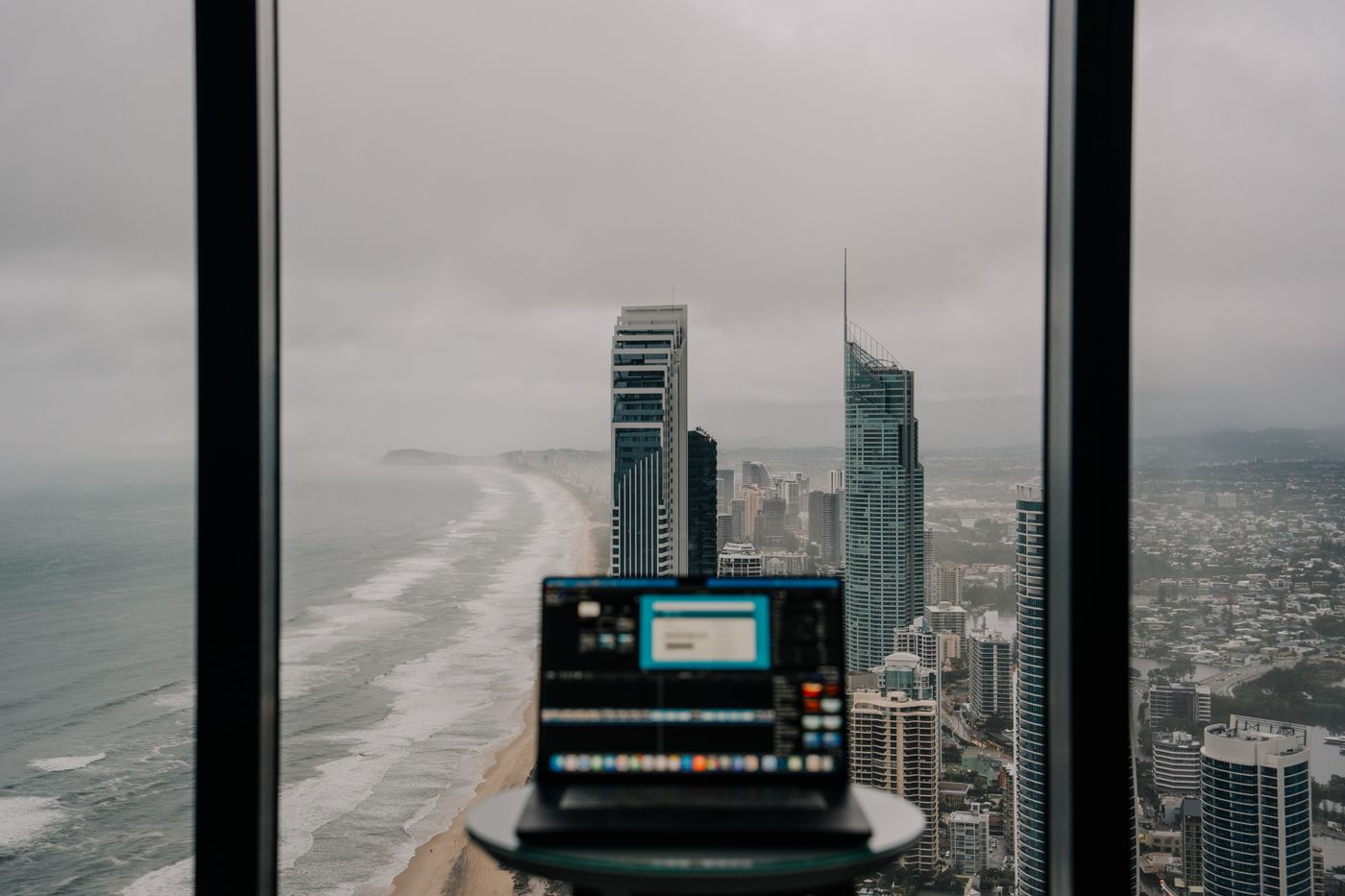 Cityscape of Gold Coast, Australia viewed from an office with a laptop, featuring skyscrapers and the coastline.