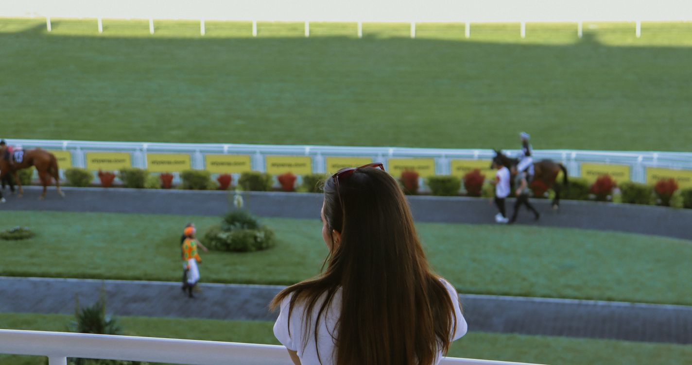 Une spectatrice observe la piste d'un hippodrome pendant que jockeys et chevaux se préparent avant une course