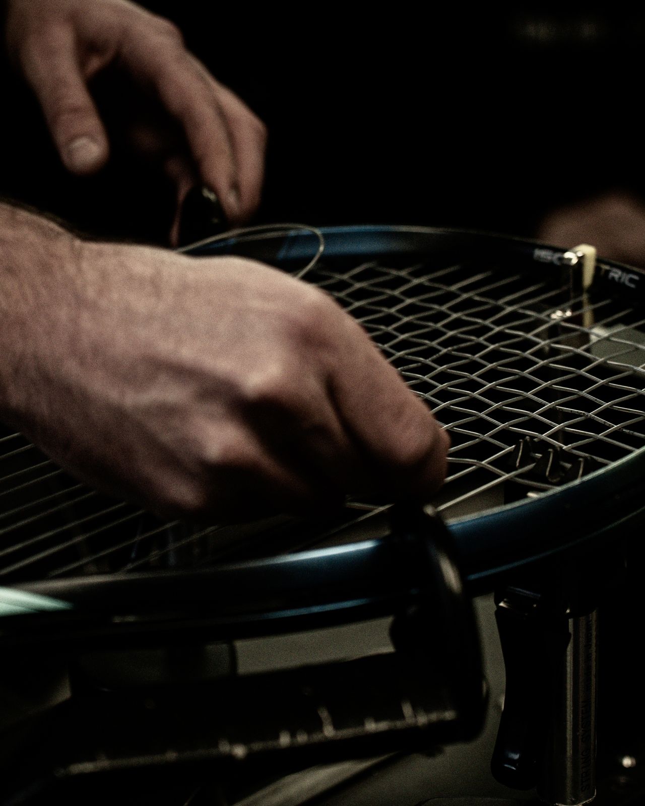 Close-up of hands weaving new string through a racquet on a stringing machine