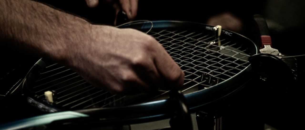 Close-up of hands weaving new string through a racquet on a stringing machine