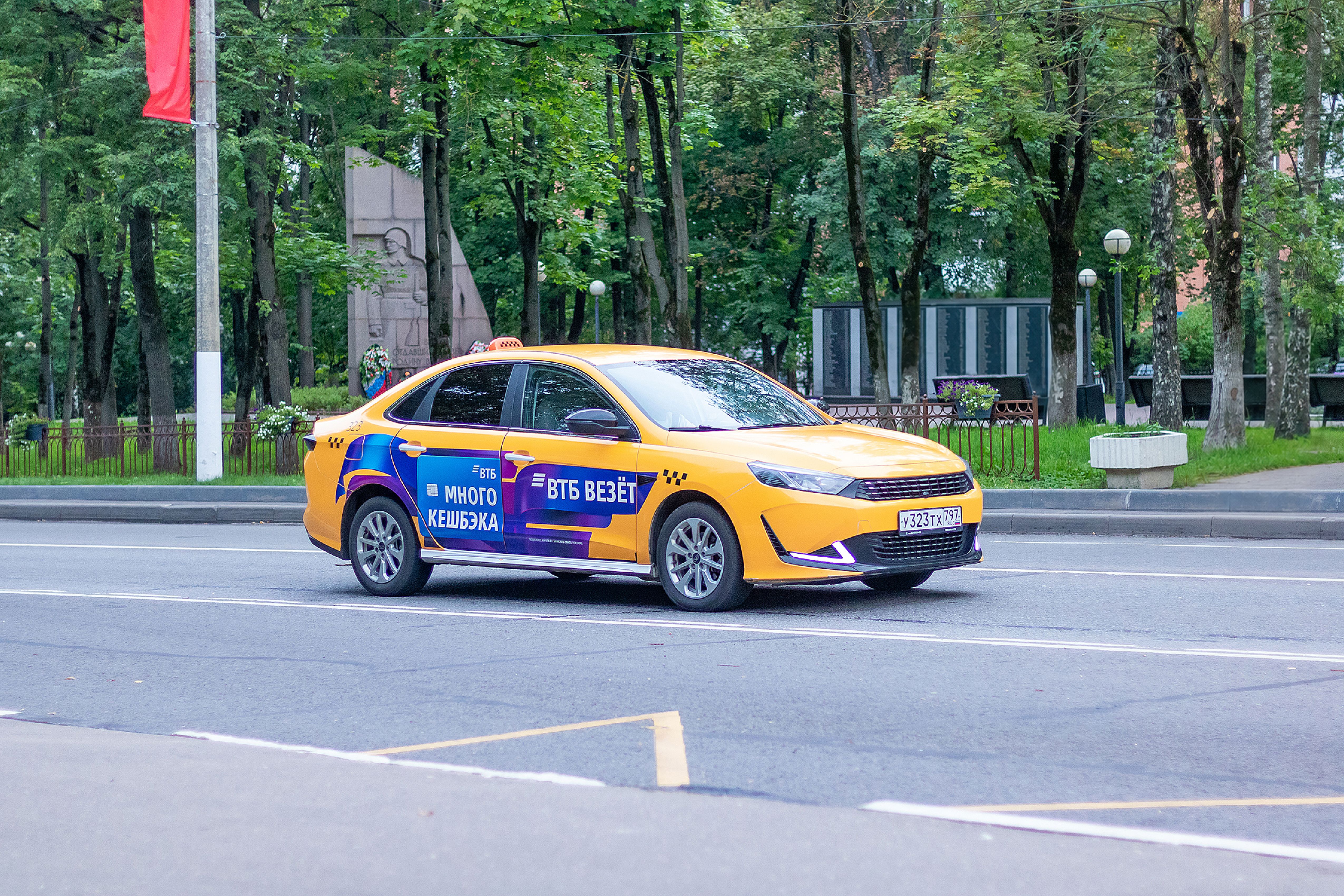 Yellow taxi driving through Krasnogorsk park in Moscow Oblast, Russia, during the day.
