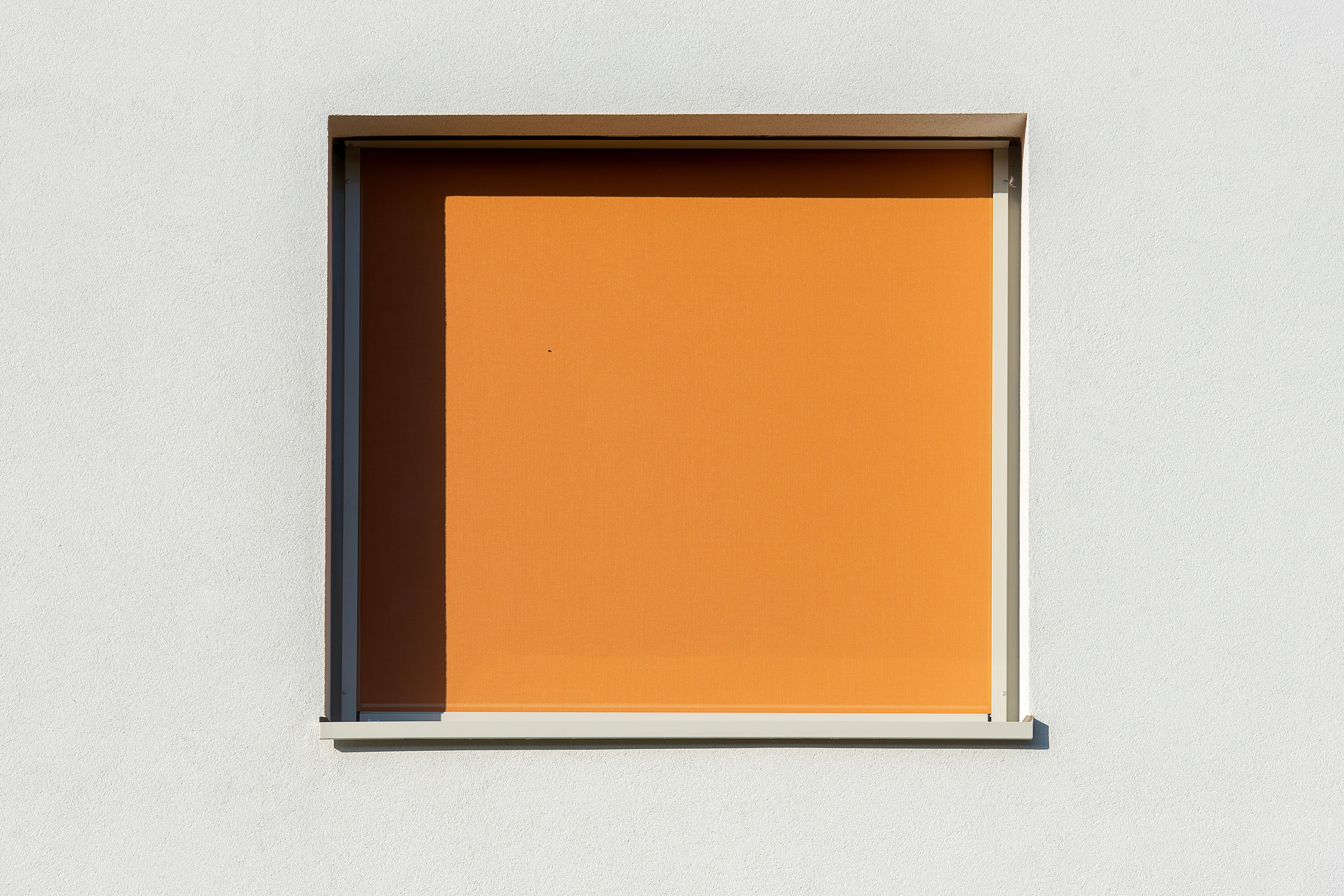 Aesthetic minimalist window with a bright orange shade on a white wall, creating strong contrast.
