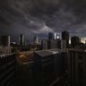 Dark storm clouds gather over a modern international city skyline at dusk.