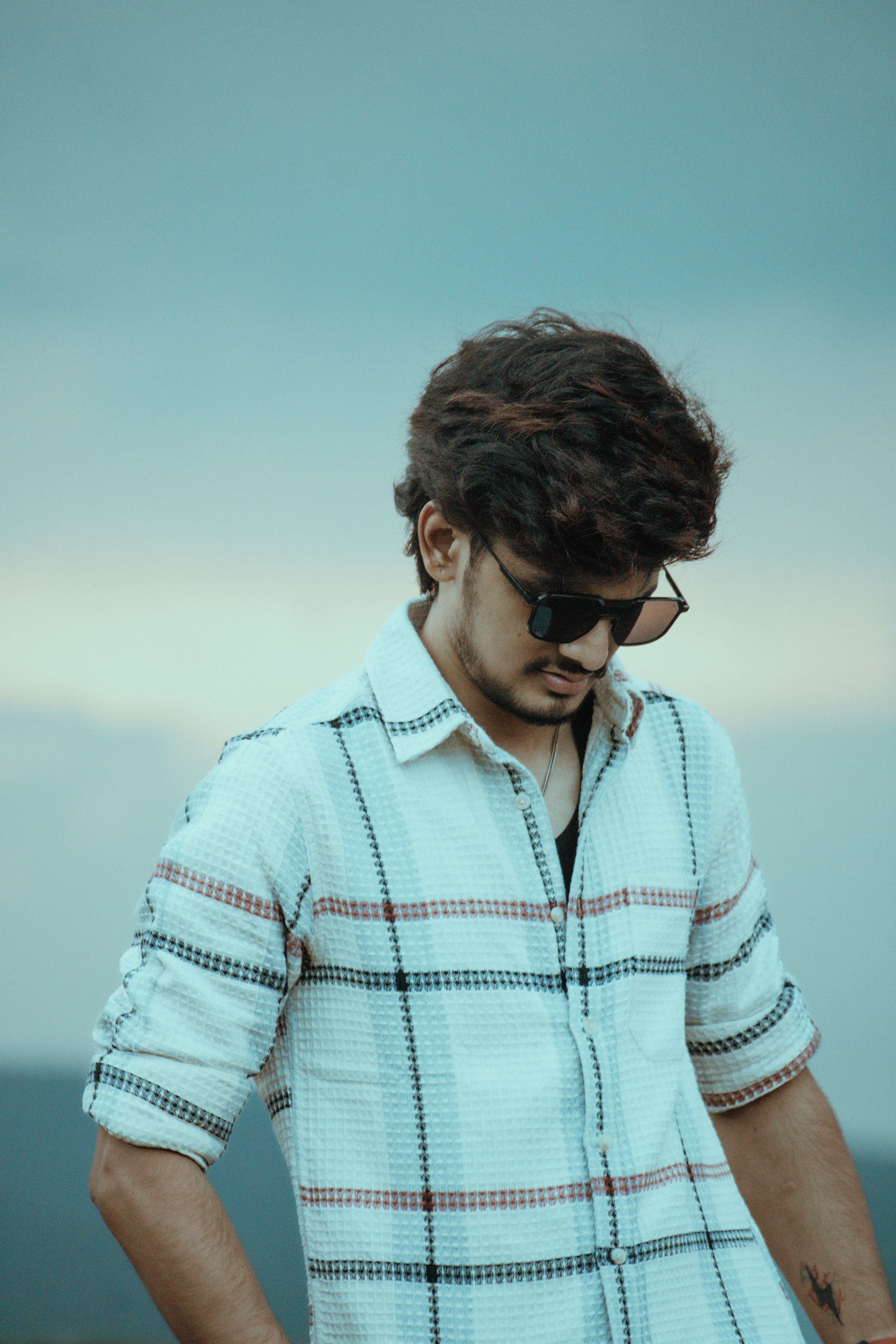 Young man wearing sunglasses and a plaid shirt, posing outdoors in Salem, India.