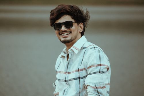 Free Portrait of a smiling man wearing sunglasses and a checkered shirt by a lake in Salem, India. Stock Photo