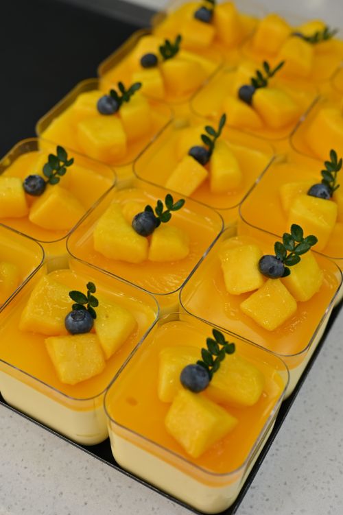 Free Vibrant mango mousse desserts topped with fresh blueberries and leaf decor in square cups. Stock Photo
