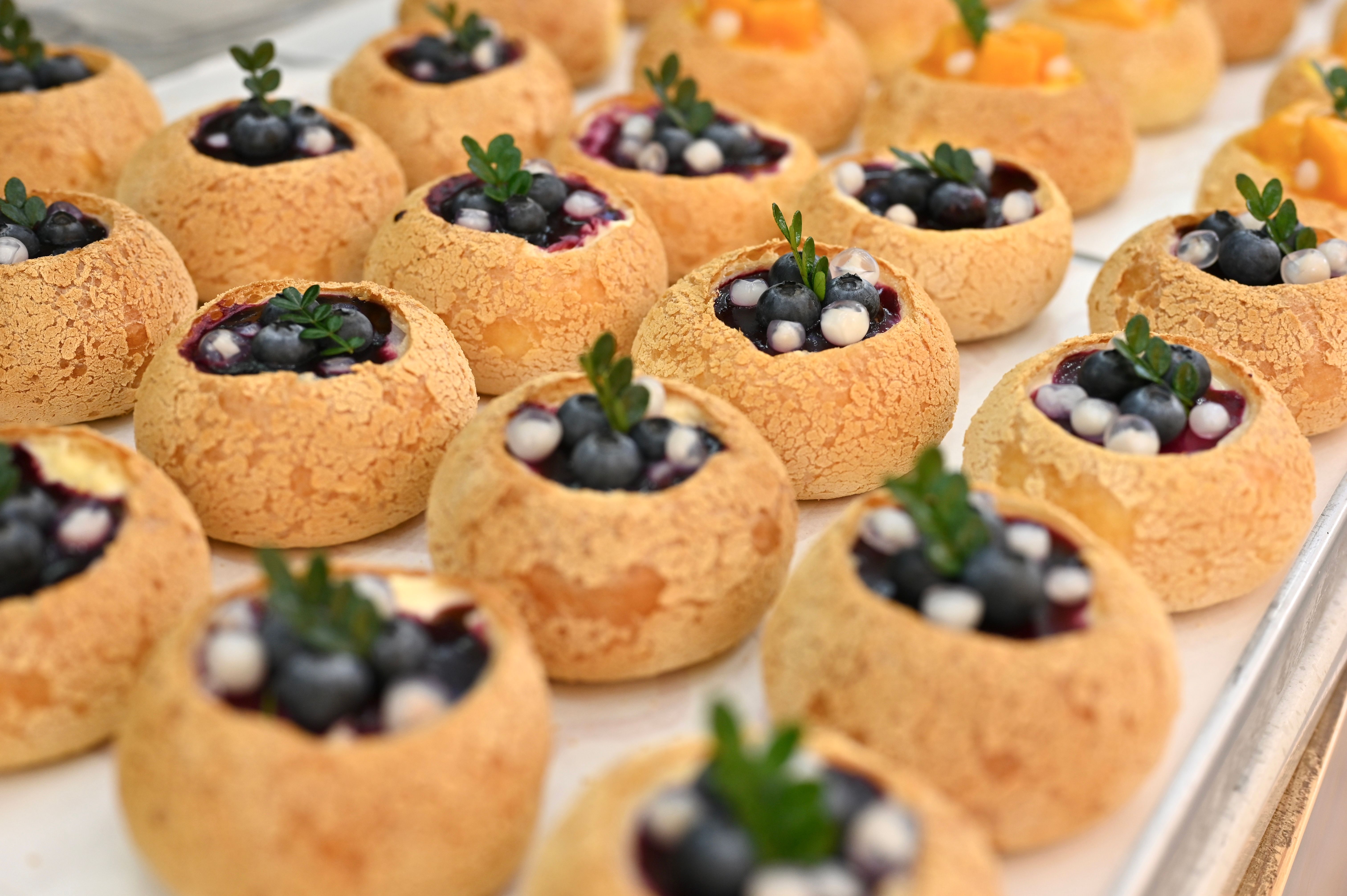 Rows of cream puffs filled with blueberries and adorned with fresh mint leaves, displayed 