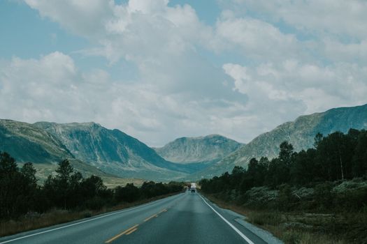 Peaceful road stretching through Norway's mountains under a vibrant blue sky, capturing nature's beauty.