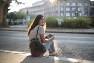 白天，一位面带微笑的女子坐在户外的人行道上，手里拿着一台平板电脑