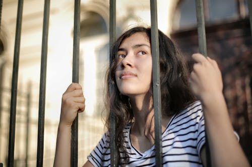 Грустная изолированная молодая женщина смотрит сквозь забор с надеждой