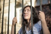 Sad isolated young woman looking away through fence with hope