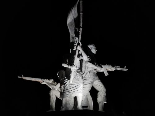 Free Striking night view of a monumental sculpture depicting armed figures holding a flag, symbolizing courage. Stock Photo
