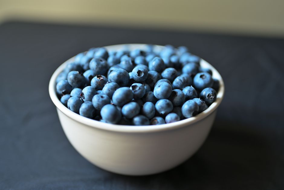A white bowl filled with fresh blueberries, overhead view