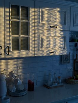 Beautiful morning sunlight creates intricate patterns on white kitchen cabinets.
