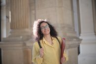Cheerful young clever student with papers and backpack on campus