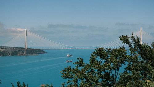 Free A stunning view of a large suspension bridge spanning over a serene blue sea, with ships passing under. Stock Photo