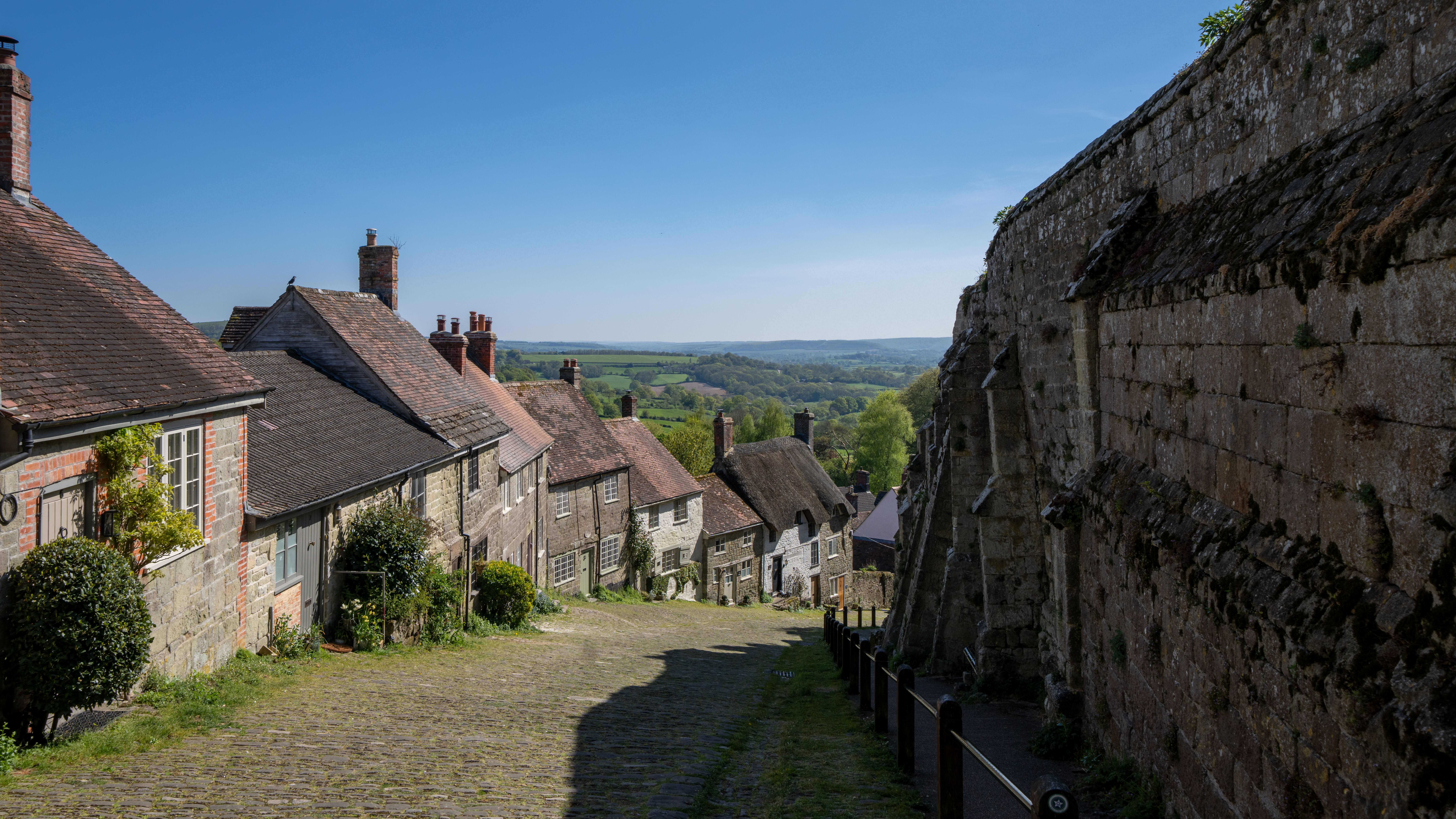 A picturesque view of Gold Hill in Shaftesbury, England, featuring historic stone cottages and a scenic countryside vista.