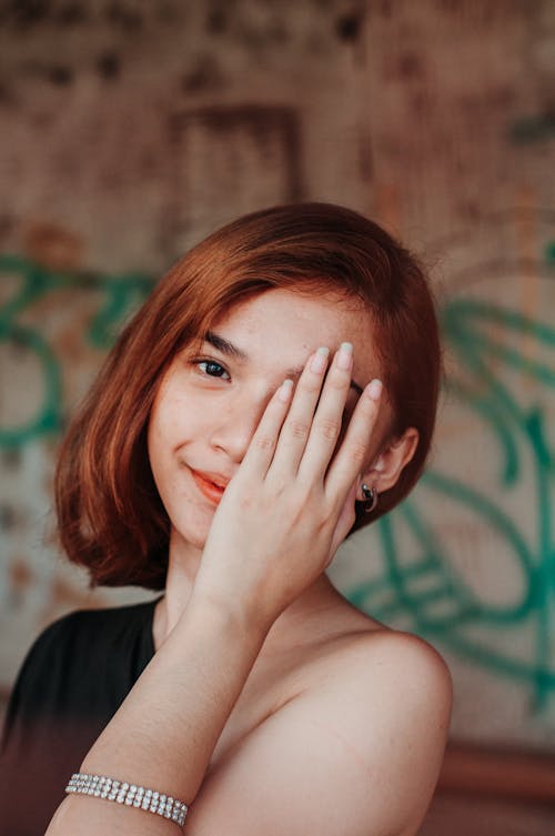 Free Tender teenage woman with short hair covering eye playfully with hand looking at camera Stock Photo