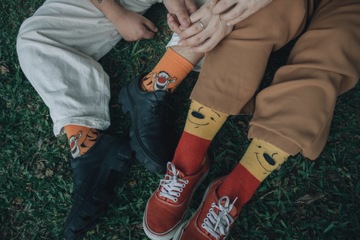 Two friends wearing playful socks sit closely on grass, showing comfort and friendship.