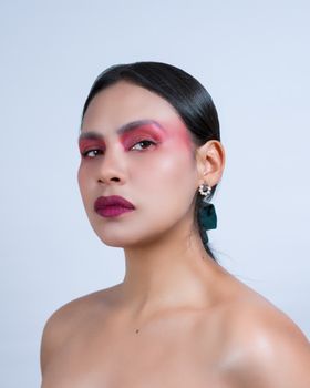 A striking portrait of a woman with bold artistic makeup and elegant earrings, set against a minimal background.